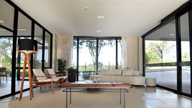 A modern living room with a sofa, chairs, a coffee table, and a large window offering a view of the outdoors. - Vallér Parque Hotel Executive (Lajeado)