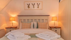 A neatly made bed with folded towels, two bedside tables with lamps, and a framed picture of rabbits on the wall.
