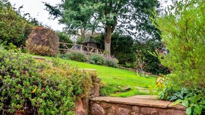 A stone staircase leading up to a garden area with a variety of plants and a gazebo in the background.