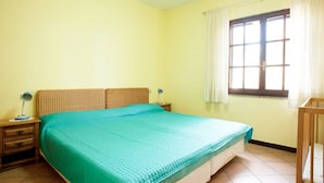 A bedroom with a large bed, a nightstand with a lamp, a window with curtains, and a crib.