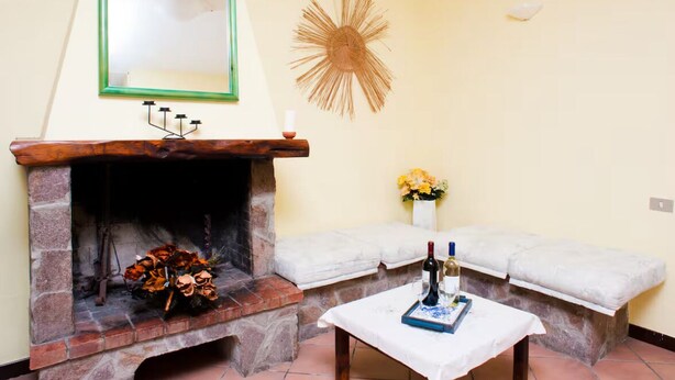 A cozy room with a stone fireplace, a mirror, a decorative sunburst wall piece, and a bench with a vase of flowers.