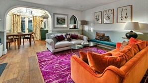 A living room with a white sofa, an orange sofa, a dining table with chairs, and a purple rug.