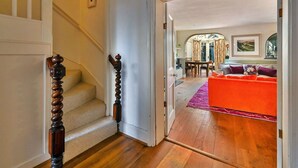 A staircase with a wooden handrail leading to a room with a red sofa and a purple rug.