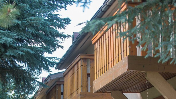 A row of wooden balconies with stone accents, outdoor seating with potted plants, and a well-maintained lawn.