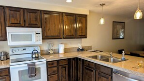 A kitchen with dark wooden cabinets, a white microwave, a stove, a sink, and a stainless steel refrigerator.