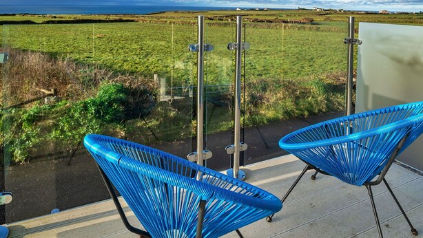 A balcony with two blue chairs, a metal railing, and a view of a green field and the sea. - Stunning  villa for 2 guests with WIFI and terrace (Tintagel)