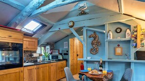 Une cuisine compacte avec des meubles en bois, un four à micro-ondes et un évier. On y trouve également un coin repas avec une table et des chaises, ainsi qu’une décoration murale représentant un hippocampe.