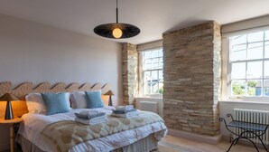 A bedroom with a stone accent wall, a bed with neatly folded towels, a bedside lamp, and a view through a window. - Beautiful  villa for 19 people with hot tub, WIFI, TV, terrace and pets allowed (Newquay)