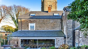 A stone building with a large garage door, a dining area with outdoor seating, and a tower with a clock. - Beautiful  villa for 19 people with hot tub, WIFI, TV, terrace and pets allowed (Newquay)