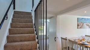 Un escalier dont les marches sont recouvertes de moquette et qui possède des balustrades noires, menant à un coin repas où une table est dressée pour deux personnes, et où un tableau représentant une scène de plage est accroché au mur.