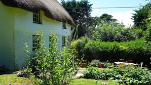 Une maison à toit de chaume avec un jardin devant.