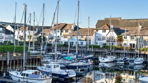 Een jachthaven met verschillende boten die aanmeren, omgeven door woongebouwen met rieten daken.