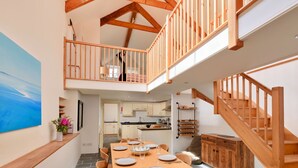A spacious dining area with a high ceiling and exposed wooden beams, a kitchen in the background, and a staircase leading to an upper level. - Beautiful  villa for 6 guests with WIFI, terrace and pets allowed (Portloe)