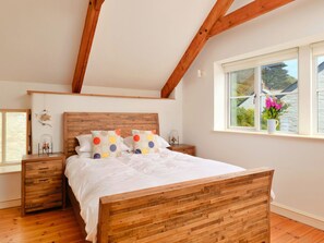 Une chambre à coucher avec un lit en bois, une table de chevet, une commode, une fenêtre donnant sur un beau paysage et une poutre en bois au plafond.