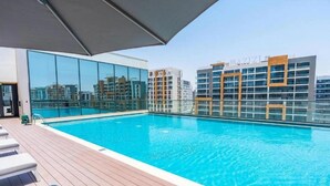 A rooftop swimming pool with clear blue water, surrounded by modern buildings and a glass barrier.