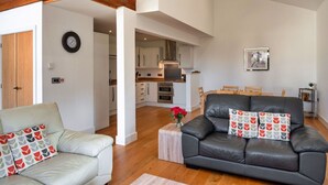 Amplia sala de estar con un sofá de cuero, un sofá blanco y una mesa de comedor. Se ve una cocina al fondo.
