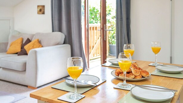 A dining area with a wooden table set for breakfast, featuring plates, glasses of orange juice, and a plate of croissants. - Lovely apartment for 3 people with terrace (Bodmin)