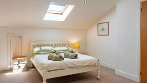 A bedroom with a skylight, a bed with rolled towels, a bedside table with a lamp, and a framed picture on the wall. - Lovely apartment for 3 people with terrace (Bodmin)