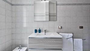 A modern bathroom with a white vanity, two sinks, a mirror, and a towel rack. - Cozy Apartment 2 steps from the Railway Station (Chirignago-Zelarino)