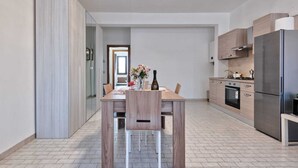 A modern kitchen with a wooden dining table, a refrigerator, and a stove. - Cozy Apartment 2 steps from the Railway Station (Chirignago-Zelarino)