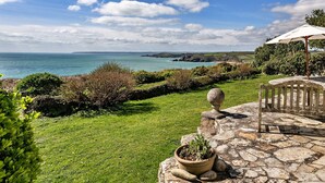A coastal garden with a stone patio, a potted plant, and a view of the sea. - Stunning  villa for 4 guests with WIFI and terrace (Germoe)