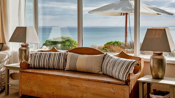 A cozy room with a wooden bench, two lamps, and a view of the sea through large windows. - Stunning  villa for 4 guests with WIFI and terrace (Germoe)
