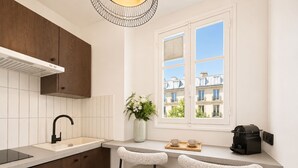 A modern kitchen with a built-in stove, a sink, and two bar stools. - 1626 Kleber (Paris)