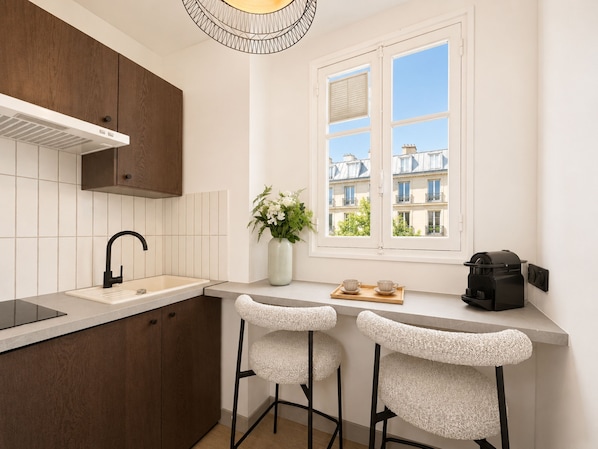 A modern kitchen with a built-in stove, a sink, and two bar stools. - 1626 Kleber (Paris)