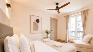 A bedroom with a bed, a sofa, a ceiling fan, a window with curtains, and a framed picture on the wall. - 1626 Kleber (Paris)
