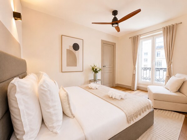 A bedroom with a bed, a sofa, a ceiling fan, a window with curtains, and a framed picture on the wall. - 1626 Kleber (Paris)