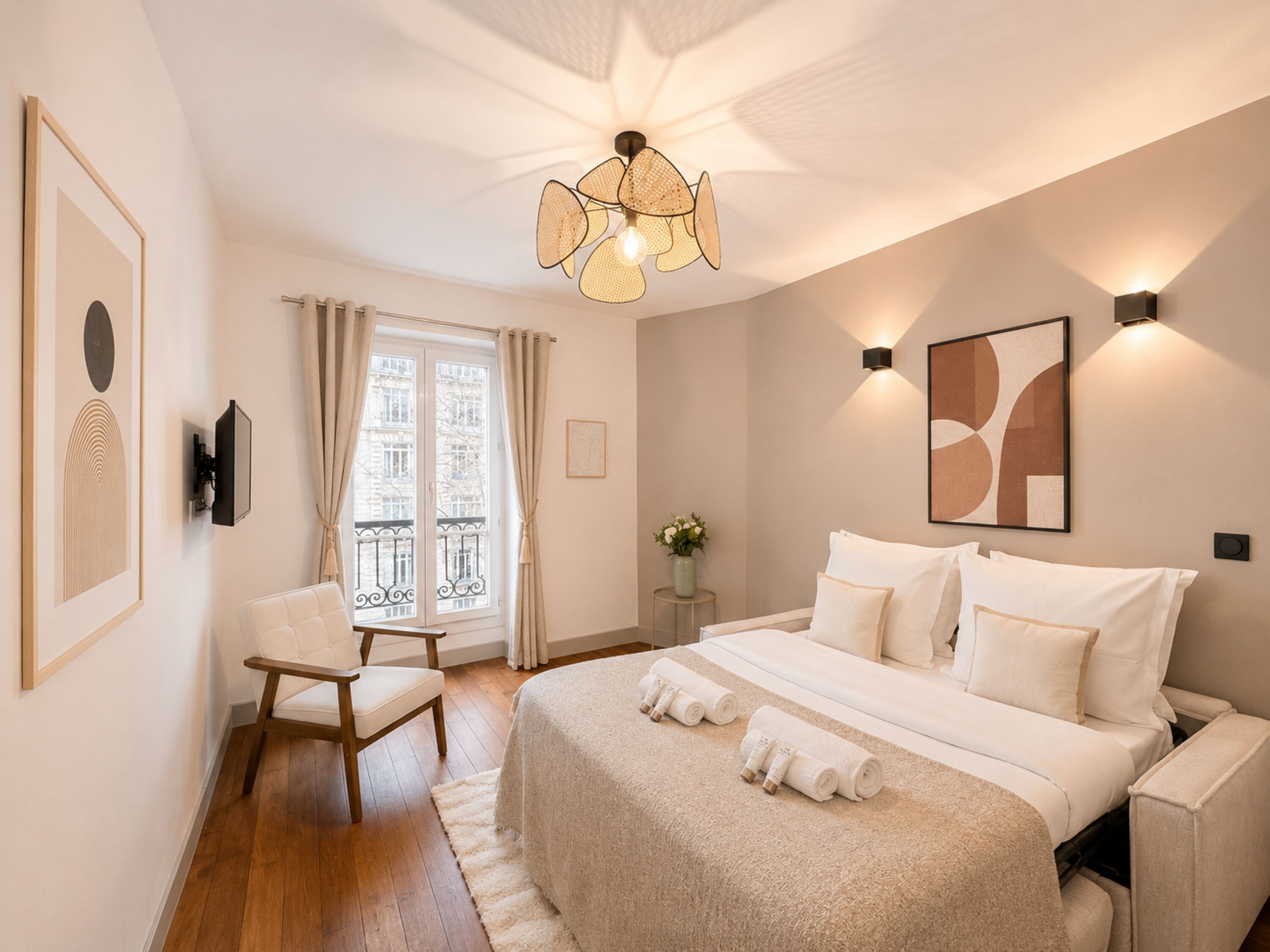 Un dormitorio con cama, una silla, una mesita de noche con un florero y una ventana con cortinas.