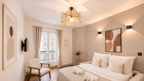 A bedroom with a bed, a chair, a bedside table with a vase, and a window with curtains. - 1626 Kleber (Paris)