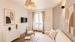A modern living room with a sofa, a coffee table, a chair, a TV, and artwork on the walls. - 1626 Kleber (Paris)