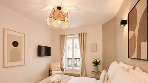 A hotel room with a bed, a TV, a window with curtains, a wall-mounted artwork, and a ceiling light fixture. - 1626 Kleber (Paris)