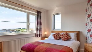 Ein Schlafzimmer mit Bett, Nachttisch, einem Fenster mit Vorhängen, einer Heizung und Blick ins Freie.