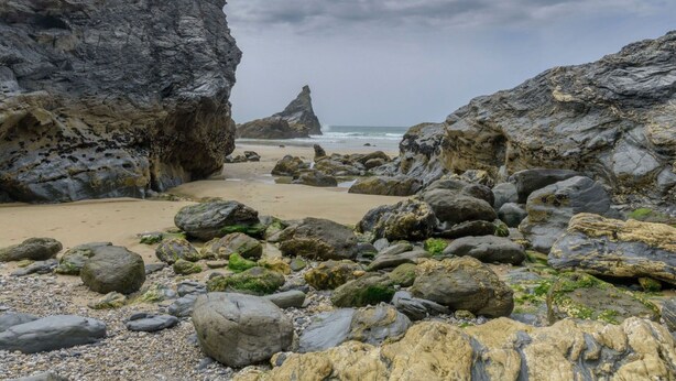 A rocky beach with large boulders and a narrow passageway leading to the sea.