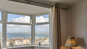 A corner room with a bay window overlooking a coastal view, a lamp on a bedside table, and a textured wall. - Beautiful apartment for 4 guests with WIFI (St Ives)
