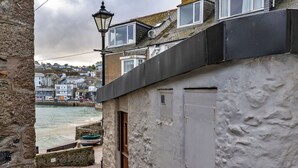 A narrow cobblestone street with a white building featuring a black awning and a small boat docked outside. - Beautiful apartment for 4 guests with WIFI (St Ives)