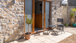Un edificio de piedra con puerta de madera y puerta corredera de vidrio, una planta en maceta y mobiliario exterior.