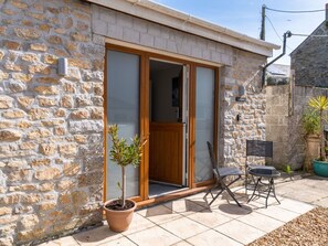 A stone building with a wooden door and a sliding glass door, a potted plant, and outdoor furniture. - Lovely apartment for 2 guests with WIFI, TV and pets allowed (Porthleven)