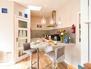 A modern kitchen with a dining area, featuring a white countertop, grey chairs, and pendant lights. - Lovely apartment for 2 guests with WIFI, TV and pets allowed (Porthleven)