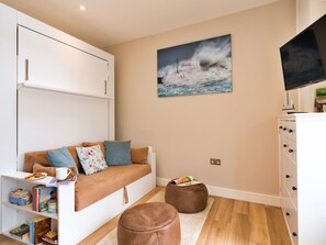 Een moderne woonkamer met een bank, poefjes, een flatscreen televisie en een schilderij van een ruige zee.