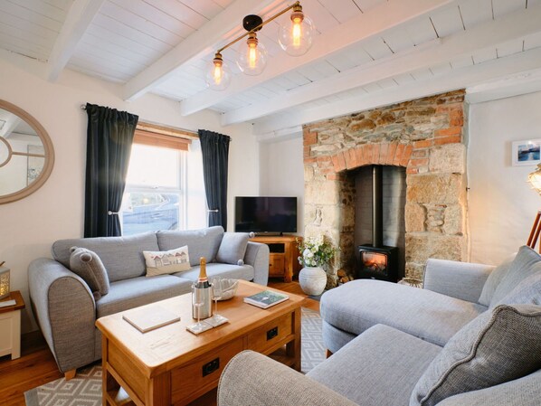 Ein gemütliches Wohnzimmer mit Kamin aus Stein, grauen Sofas, einem Holztisch und einem Fernseher.