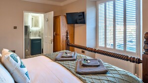 Een slaapkamer met een bed, een televisie aan de muur, een raam met zonwering en een deur naar een badkamer.