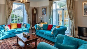 Een ruime woonkamer met twee blauwe banken, een houten salontafel en een groot raam met gordijnen.
