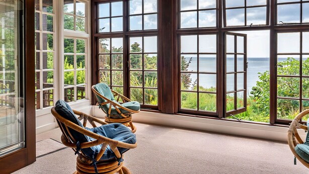 Una habitación con ventanas amplias que dan al mar, sillas de mimbre y un candelabro.