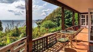 Un espacio al aire libre techado con una mesa y sillas, con vistas panorámicas al mar y la vegetación.