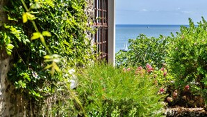 Un edificio costero con vista al mar, rodeado de vegetación exuberante y plantas con flores.