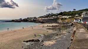 Una playa costera con un litoral rocoso, un paseo marítimo pavimentado y edificios al fondo.