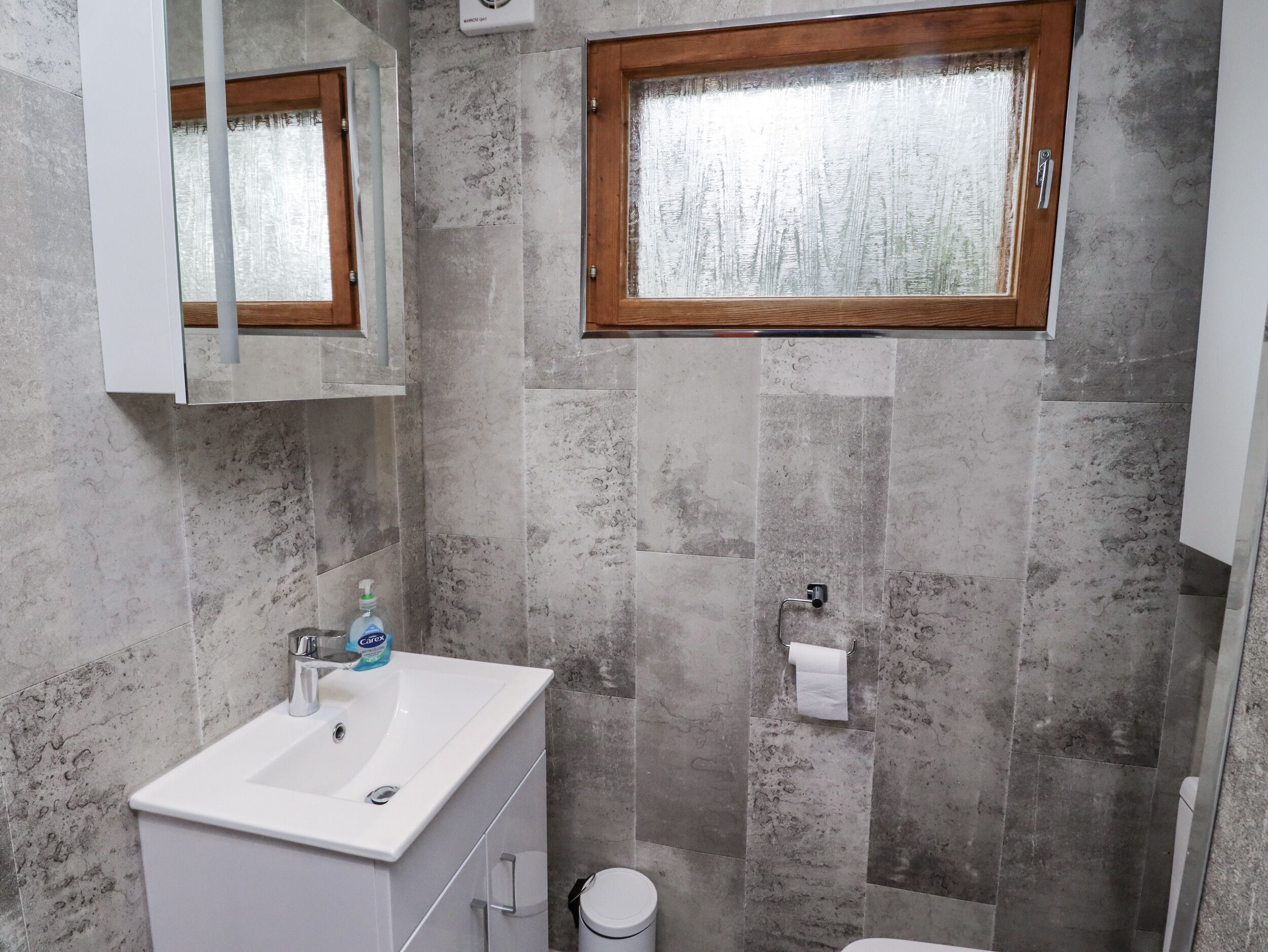 Un baño con lavamanos blanco, un espejo, una ventana y un inodoro.
